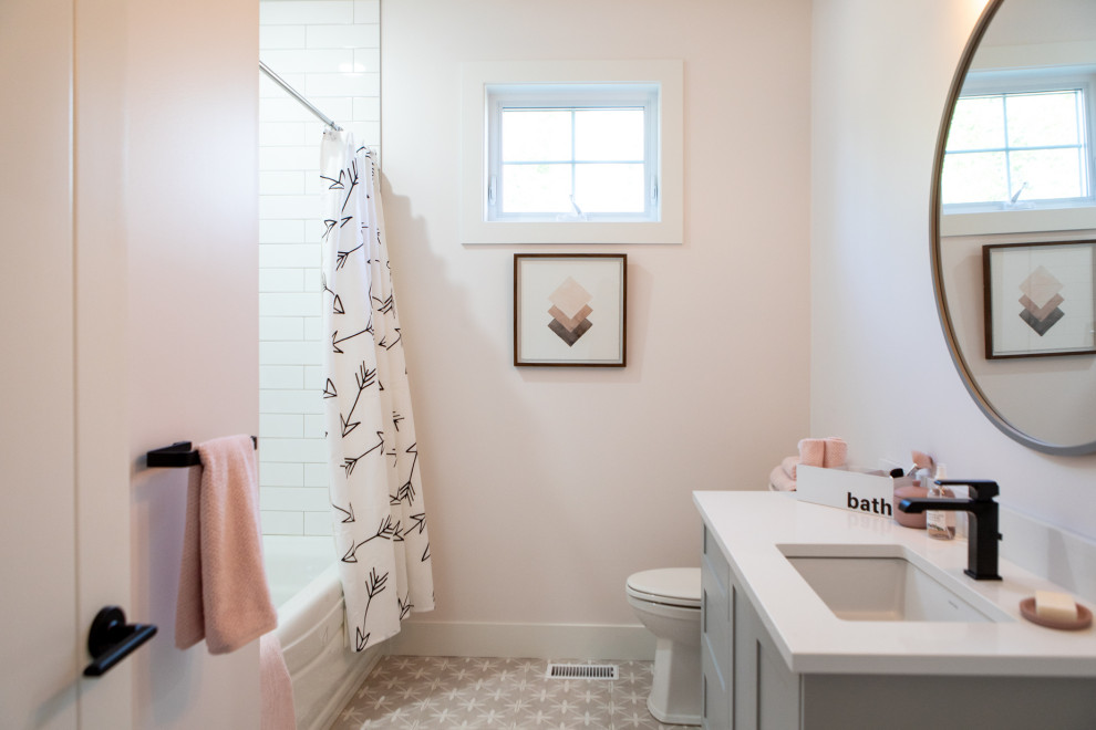 This is an example of a medium sized scandinavian family bathroom in Other with shaker cabinets, grey cabinets, an alcove bath, white tiles, metro tiles, pink walls, ceramic flooring, a submerged sink, solid surface worktops, grey floors and white worktops.