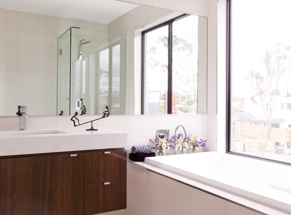 Modelo de cuarto de baño actual con armarios con paneles lisos, puertas de armario de madera en tonos medios, bañera empotrada y ventanas