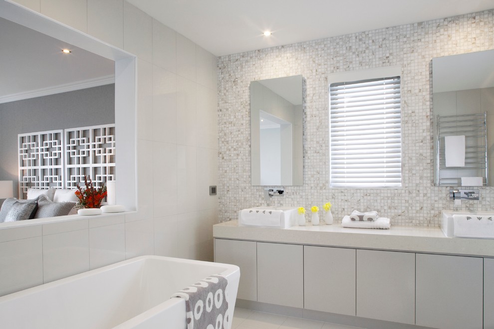 На фото: ванная комната в современном стиле с настольной раковиной, плоскими фасадами, белыми фасадами, отдельно стоящей ванной и белой плиткой с