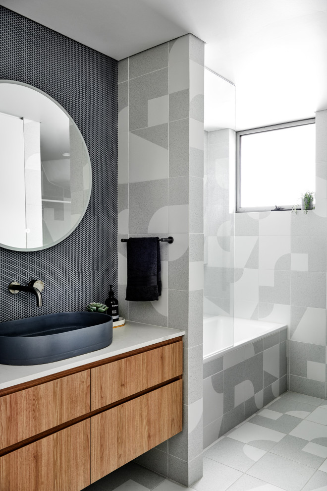 Inspiration for a medium sized scandi bathroom in Sydney with medium wood cabinets, a built-in bath, a shower/bath combination, blue tiles, porcelain tiles, porcelain flooring, a vessel sink, engineered stone worktops and grey floors.