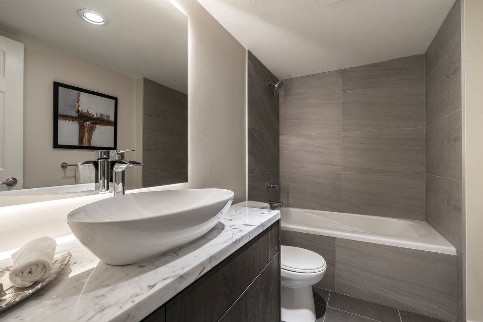 Cette photo montre une salle de bain moderne en bois foncé avec un placard à porte plane, une baignoire posée, un carrelage beige, des carreaux de béton, un sol en carrelage de porcelaine, une vasque, un plan de toilette en marbre et un sol noir.