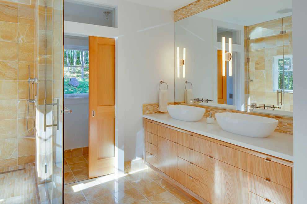 Example of a large trendy master beige tile and porcelain tile marble floor bathroom design in Portland Maine with a vessel sink, flat-panel cabinets, light wood cabinets, a one-piece toilet, beige walls and solid surface countertops