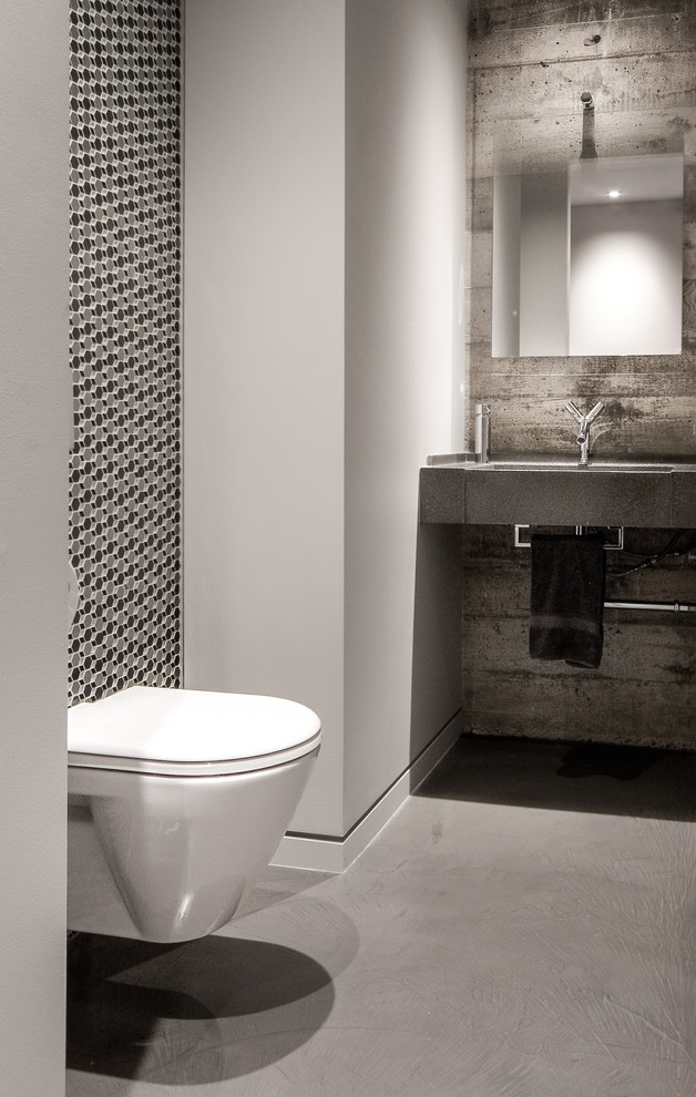 Idée de décoration pour une salle d'eau urbaine de taille moyenne avec un carrelage gris, un carrelage noir, sol en béton ciré, un lavabo encastré, WC suspendus, mosaïque, un mur gris et un plan de toilette en béton.