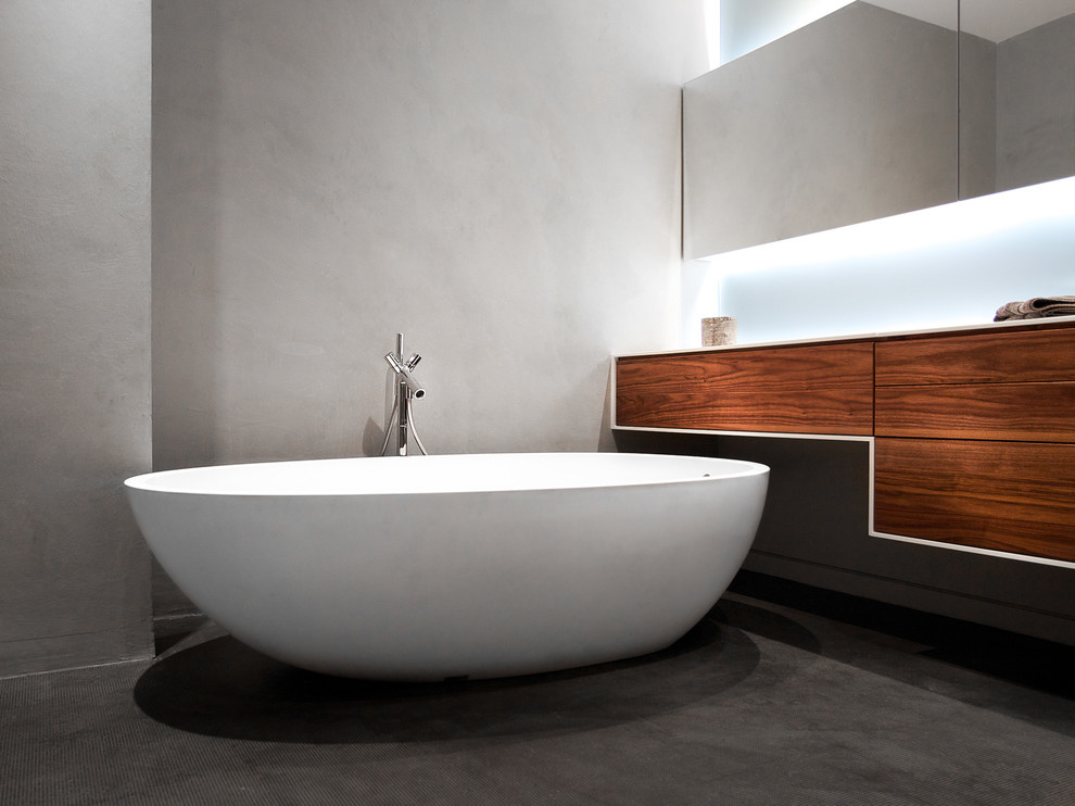 Modern inredning av ett litet en-suite badrum, med ett fristående badkar, grå kakel, klinkergolv i porslin, ett undermonterad handfat, bänkskiva i akrylsten, släta luckor, skåp i mellenmörkt trä och grå väggar