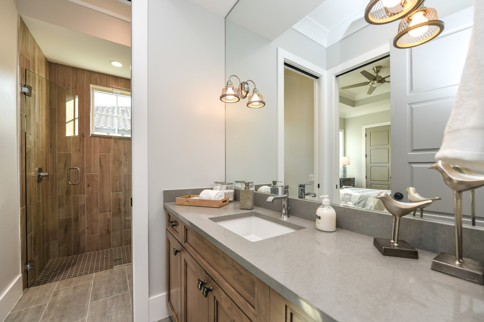 Design ideas for a medium sized traditional family bathroom in Tampa with recessed-panel cabinets, light wood cabinets, an alcove shower, brown tiles, porcelain tiles, grey walls, medium hardwood flooring, a submerged sink, brown floors and a hinged door.