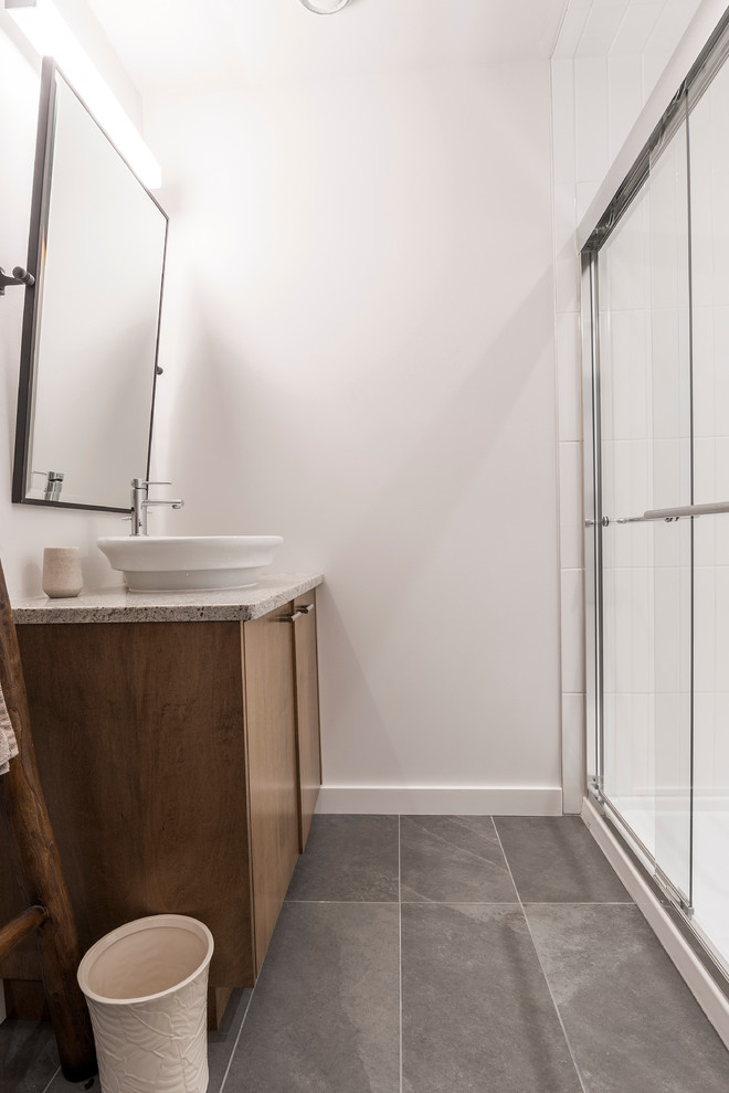 Kleines Modernes Duschbad mit Toilette mit Aufsatzspülkasten, weißen Fliesen, Keramikfliesen, weißer Wandfarbe, Keramikboden, Einbauwaschbecken, Granit-Waschbecken/Waschtisch, flächenbündigen Schrankfronten, hellbraunen Holzschränken, Duschnische, grauem Boden und Schiebetür-Duschabtrennung in Montreal