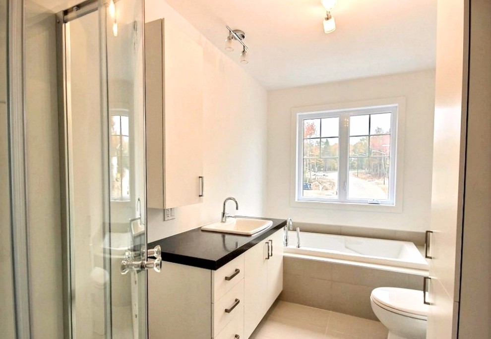 This is an example of a medium sized contemporary ensuite bathroom in Other with flat-panel cabinets, white cabinets, a corner bath, a corner shower, a one-piece toilet, beige tiles, ceramic tiles, white walls, ceramic flooring, a built-in sink, solid surface worktops, beige floors, a sliding door and black worktops.