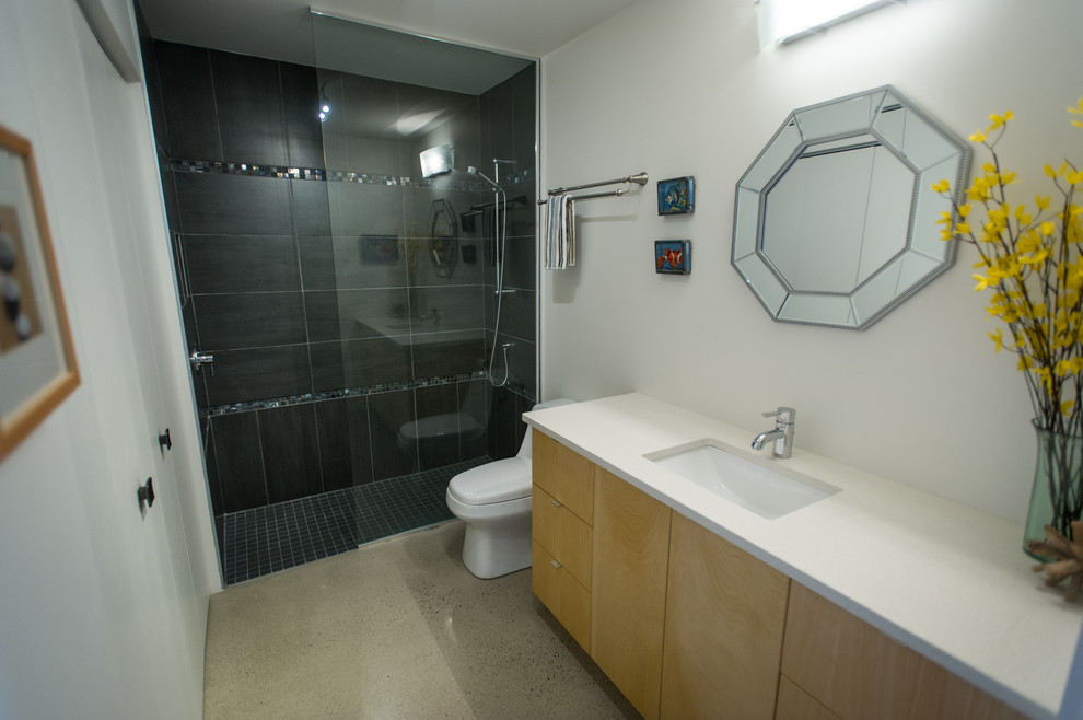 This is an example of a medium sized contemporary bathroom in Montreal with a submerged sink, flat-panel cabinets, light wood cabinets, quartz worktops, a freestanding bath, a corner shower, a one-piece toilet, beige tiles, white walls and concrete flooring.