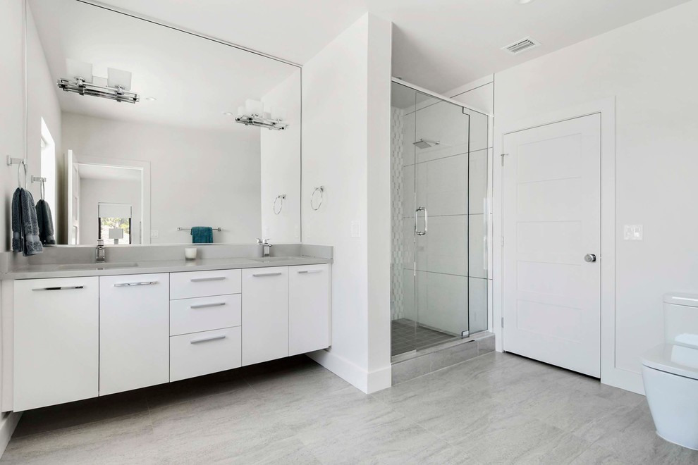 Exemple d'une salle de bain moderne de taille moyenne avec un placard à porte plane, des portes de placard blanches, WC à poser, un carrelage gris, des carreaux de porcelaine, un mur blanc, un sol en carrelage de porcelaine, un lavabo encastré et un plan de toilette en quartz modifié.