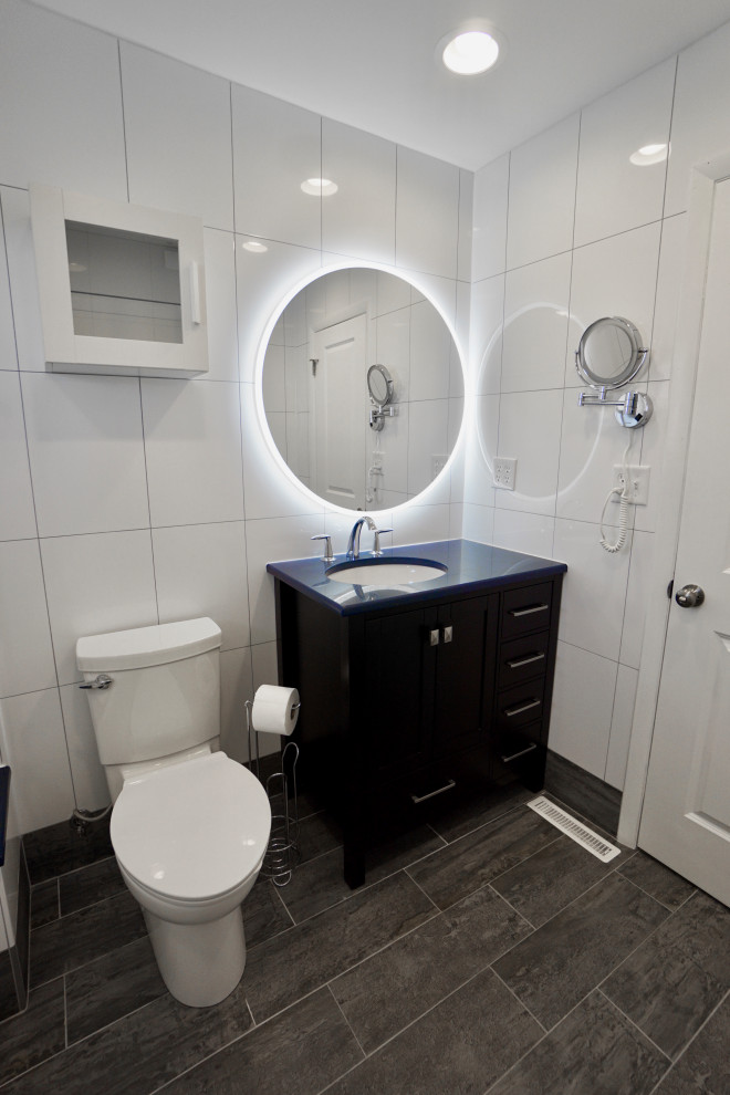 Cette image montre une petite salle de bain principale design avec un placard à porte shaker, des portes de placard noires, une baignoire en alcôve, un combiné douche/baignoire, WC à poser, un carrelage blanc, des carreaux de céramique, un mur blanc, un sol en carrelage de céramique, un lavabo encastré, un plan de toilette en quartz, un sol gris, une cabine de douche à porte coulissante, un plan de toilette bleu, un banc de douche, meuble simple vasque et meuble-lavabo sur pied.