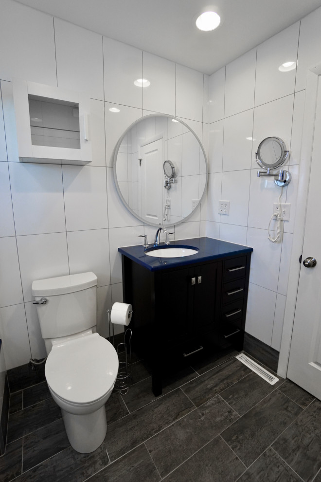 Пример оригинального дизайна: маленькая главная ванная комната в современном стиле с фасадами в стиле шейкер, черными фасадами, ванной в нише, душем над ванной, унитазом-моноблоком, белой плиткой, керамической плиткой, белыми стенами, полом из керамической плитки, врезной раковиной, столешницей из кварцита, серым полом, душем с раздвижными дверями, синей столешницей, сиденьем для душа, тумбой под одну раковину и напольной тумбой для на участке и в саду