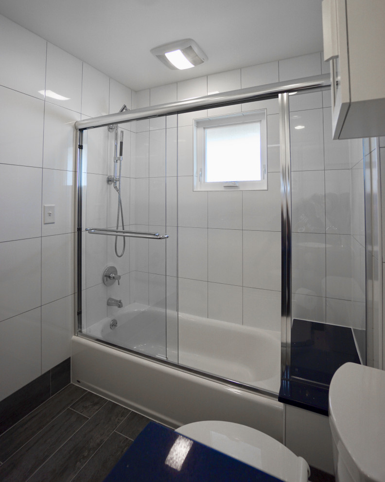 На фото: маленькая главная ванная комната в современном стиле с фасадами в стиле шейкер, черными фасадами, ванной в нише, душем над ванной, унитазом-моноблоком, белой плиткой, керамической плиткой, белыми стенами, полом из керамической плитки, врезной раковиной, столешницей из кварцита, серым полом, душем с раздвижными дверями, синей столешницей, сиденьем для душа, тумбой под одну раковину и напольной тумбой для на участке и в саду