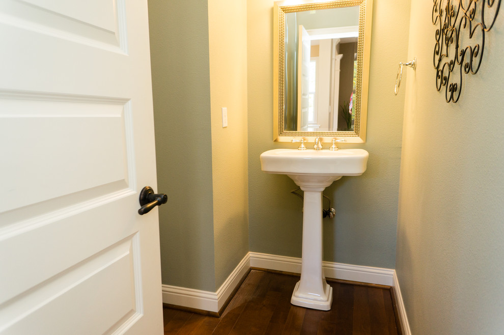 Modelo de cuarto de baño de estilo americano pequeño con lavabo con pedestal, paredes verdes, suelo de madera en tonos medios y aseo y ducha