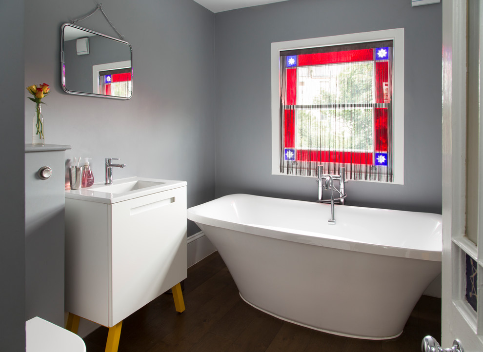 Immagine di una stanza da bagno padronale minimal con ante lisce, ante bianche, vasca freestanding, pareti grigie, parquet scuro, lavabo integrato e pavimento marrone