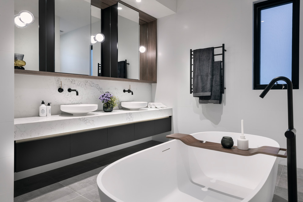 Источник вдохновения для домашнего уюта: главная ванная комната в современном стиле с плоскими фасадами, черными фасадами, отдельно стоящей ванной, белыми стенами, настольной раковиной, серым полом и белой столешницей