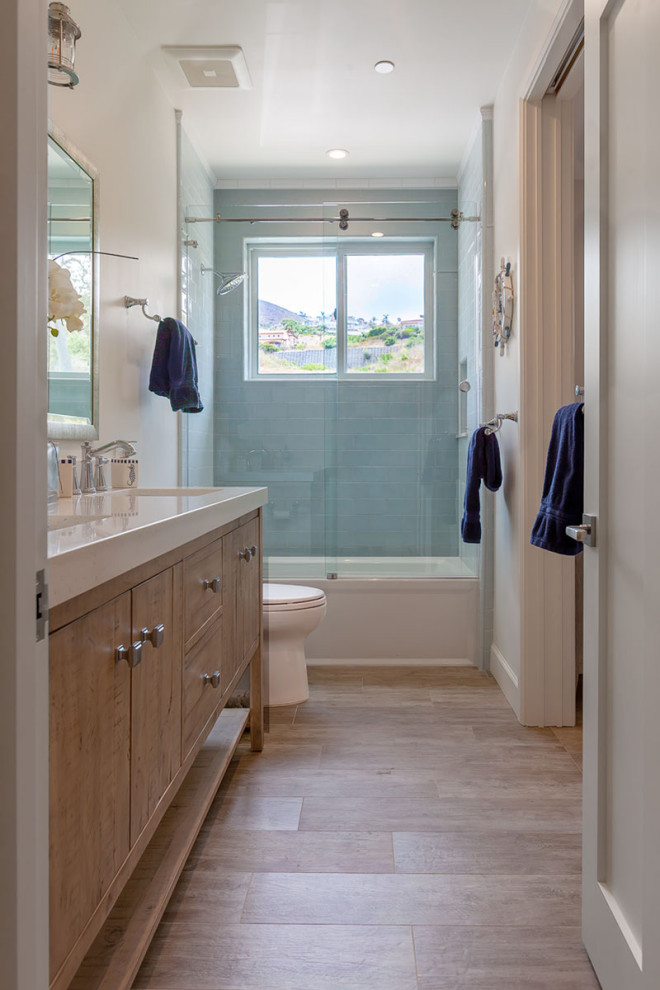 Design ideas for a medium sized beach style family bathroom in Los Angeles with shaker cabinets, distressed cabinets, an alcove bath, a shower/bath combination, blue tiles, porcelain tiles, white walls, porcelain flooring, a submerged sink, engineered stone worktops, grey floors, a sliding door, white worktops, a wall niche, double sinks, a freestanding vanity unit and a one-piece toilet.