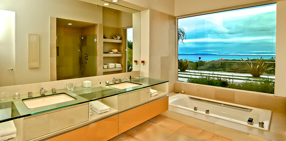 Идея дизайна: главная ванная комната в стиле модернизм с плоскими фасадами, светлыми деревянными фасадами, стеклянной столешницей, накладной ванной и полом из известняка