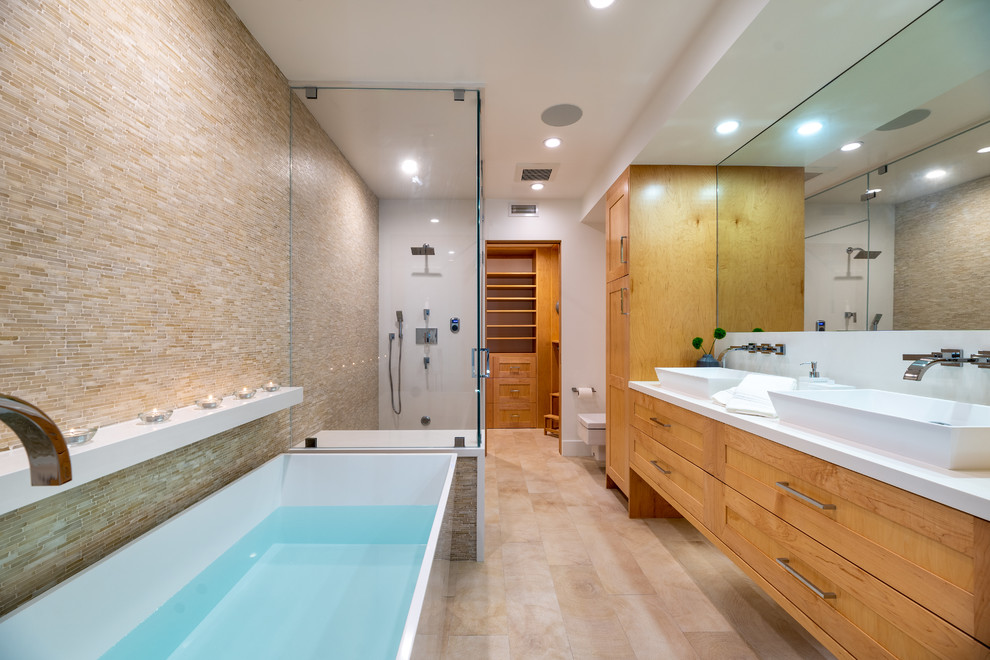Design ideas for an expansive contemporary bathroom in Los Angeles with shaker cabinets, light wood cabinets, a freestanding bath, a wall mounted toilet, beige tiles, stone tiles, white walls, porcelain flooring, a vessel sink, engineered stone worktops, beige floors and white worktops.