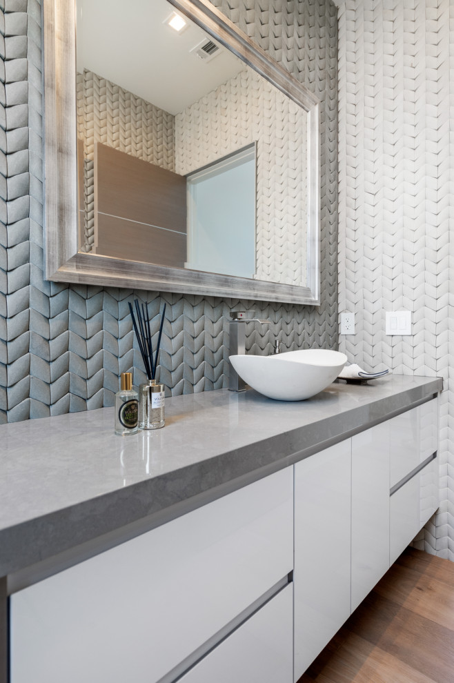 Example of a mid-sized trendy gray tile light wood floor and brown floor bathroom design in Los Angeles with flat-panel cabinets, white cabinets, a vessel sink and gray countertops