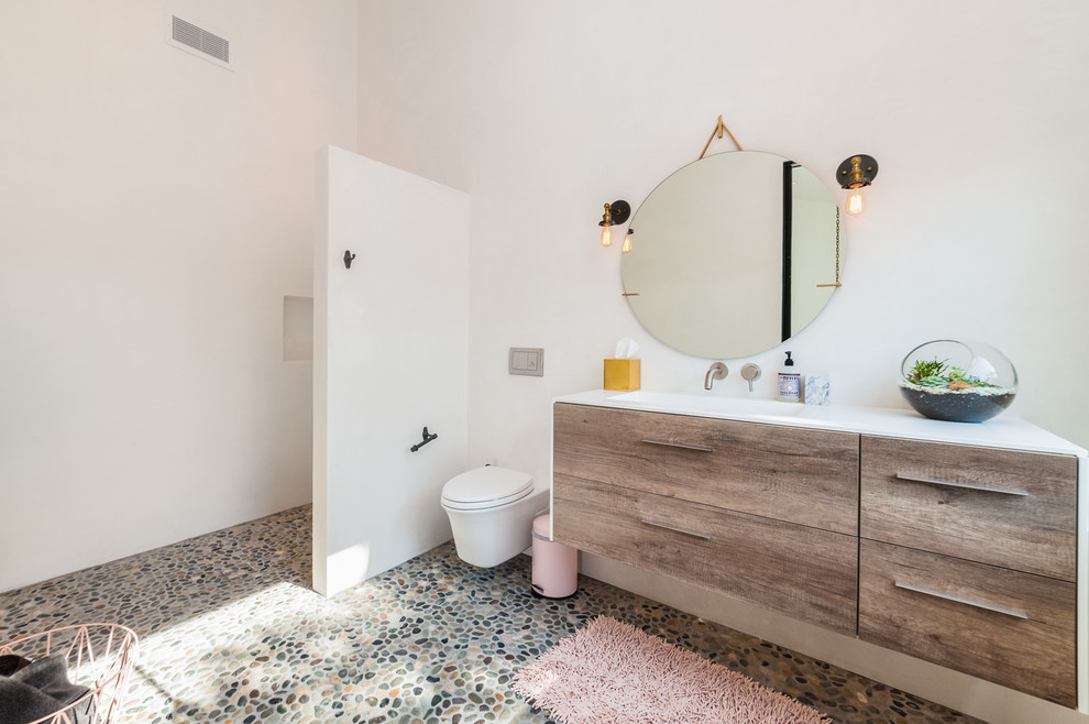 Exempel på ett stort modernt badrum med dusch, med en öppen dusch, vita väggar, klinkergolv i småsten, ett integrerad handfat, med dusch som är öppen, släta luckor, skåp i mellenmörkt trä, en bidé och bänkskiva i akrylsten