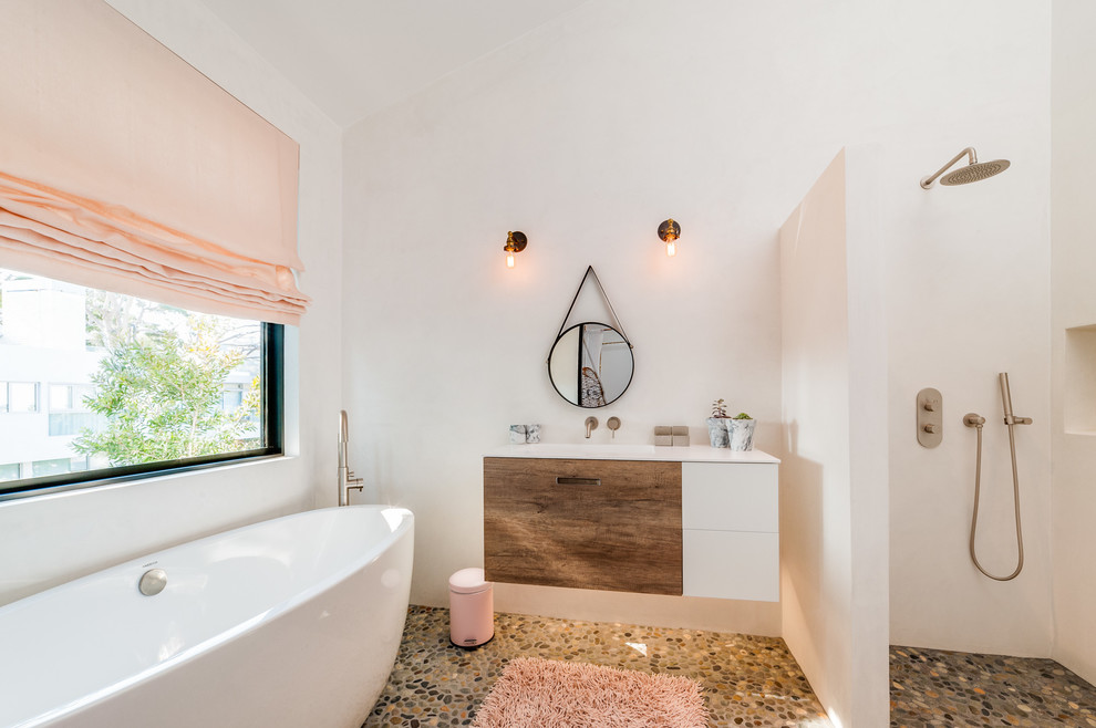 Пример оригинального дизайна: большая главная ванная комната в современном стиле с открытым душем, белыми стенами, полом из галечной плитки, монолитной раковиной, открытым душем, плоскими фасадами, фасадами цвета дерева среднего тона, отдельно стоящей ванной и столешницей из искусственного камня