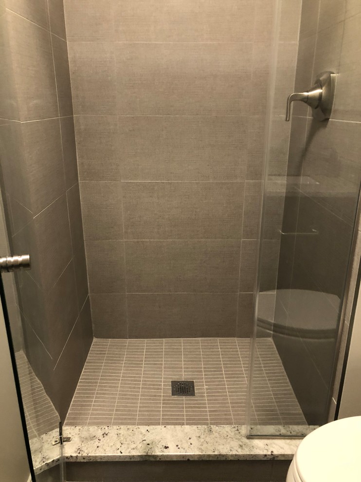 Modern inredning av ett litet badrum med dusch, med luckor med upphöjd panel, skåp i mörkt trä, en dusch i en alkov, en toalettstol med separat cisternkåpa, grå kakel, porslinskakel, grå väggar, klinkergolv i porslin, ett undermonterad handfat, granitbänkskiva, grått golv och dusch med gångjärnsdörr