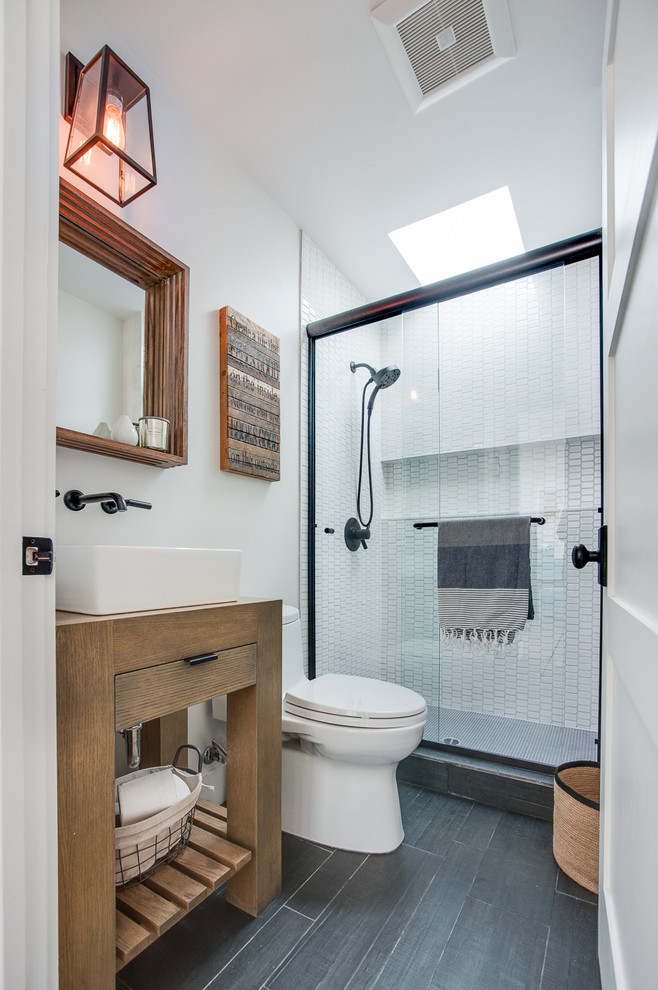 Cette photo montre une salle d'eau bord de mer en bois clair avec un placard à porte plane, une baignoire d'angle, un carrelage blanc, des plaques de verre, un mur bleu, un lavabo posé, WC à poser et une cabine de douche à porte coulissante.