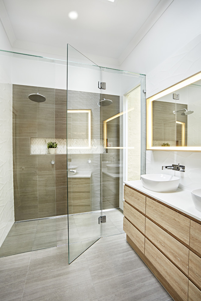 Modernes Badezimmer mit flächenbündigen Schrankfronten, hellen Holzschränken, bodengleicher Dusche, braunen Fliesen, weißen Fliesen, weißer Wandfarbe, Aufsatzwaschbecken, grauem Boden, Falttür-Duschabtrennung und weißer Waschtischplatte in Melbourne