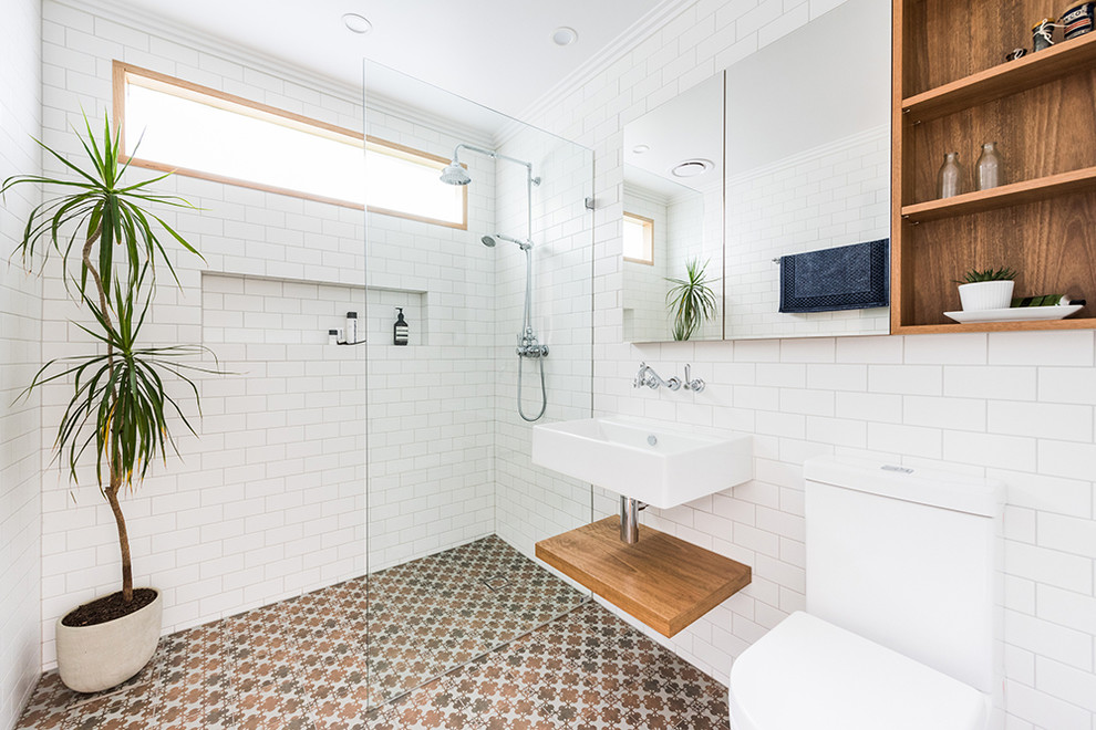 Пример оригинального дизайна: ванная комната среднего размера в современном стиле с открытыми фасадами, фасадами цвета дерева среднего тона, унитазом-моноблоком, белой плиткой, керамогранитной плиткой, белыми стенами, полом из керамогранита, душевой кабиной, подвесной раковиной, коричневым полом, открытым душем и душевой комнатой