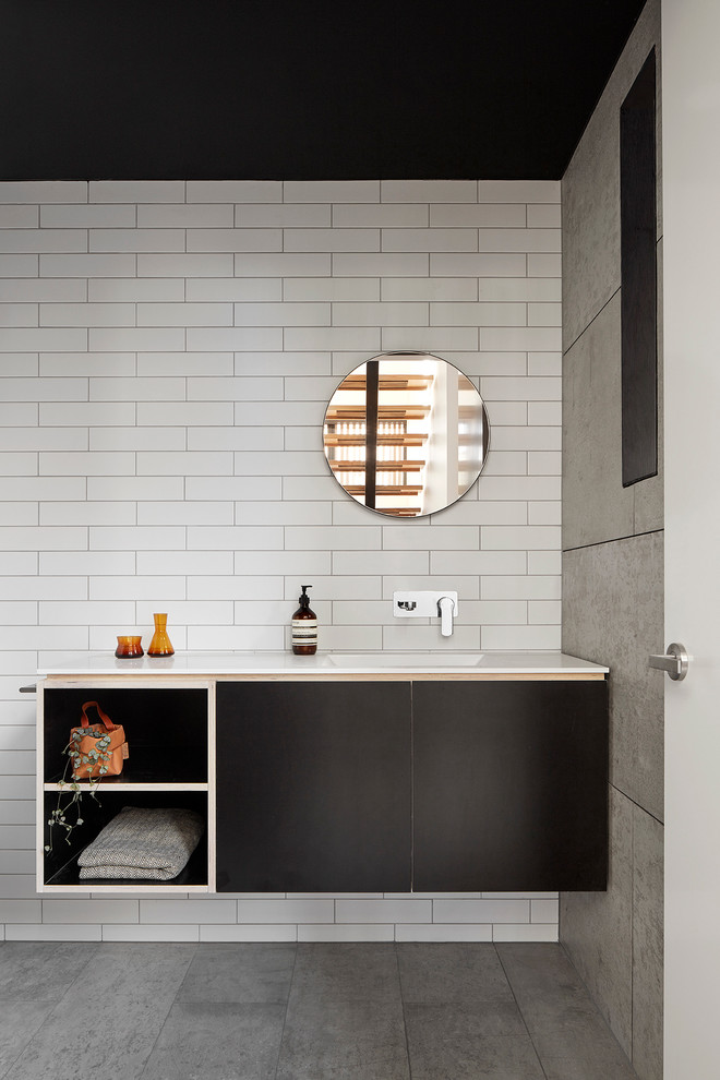 Cette image montre une salle de bain design avec un placard à porte plane, des portes de placard noires, un mur blanc et un lavabo intégré.