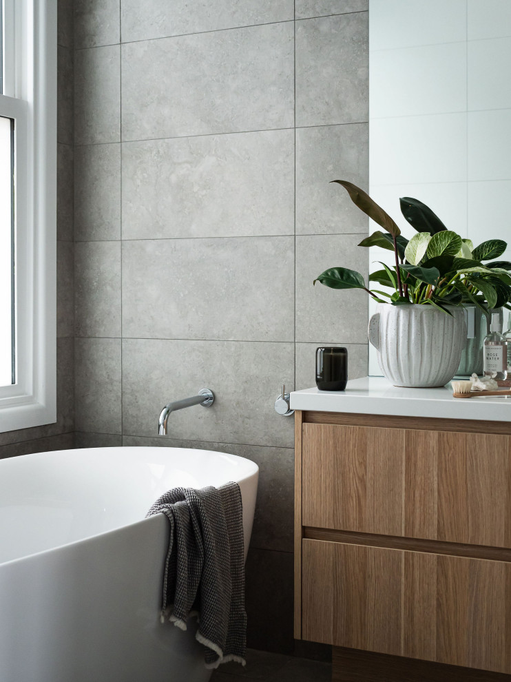Inspiration för mellanstora moderna vitt badrum med dusch, med ett fristående badkar, en toalettstol med hel cisternkåpa, grått golv, dusch med gångjärnsdörr, släta luckor, skåp i mellenmörkt trä och grå kakel