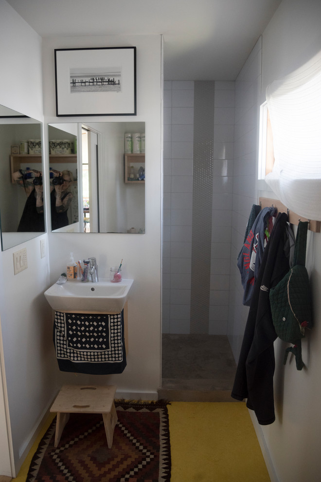 Inredning av ett skandinaviskt badrum, med öppna hyllor, skåp i ljust trä, en dusch i en alkov, en toalettstol med separat cisternkåpa, vita väggar, ett väggmonterat handfat, gult golv och med dusch som är öppen