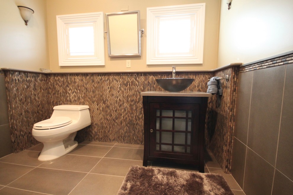 Idéer för funkis badrum, med ett fristående handfat, luckor med glaspanel, skåp i mörkt trä, en toalettstol med hel cisternkåpa och grå kakel