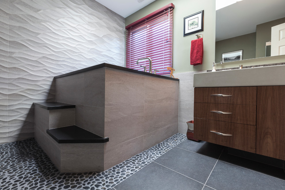 Bild på ett mellanstort funkis en-suite badrum, med ett avlångt handfat, släta luckor, skåp i mellenmörkt trä, bänkskiva i betong, ett japanskt badkar, en kantlös dusch, en toalettstol med separat cisternkåpa, svart kakel, porslinskakel, grå väggar och klinkergolv i porslin