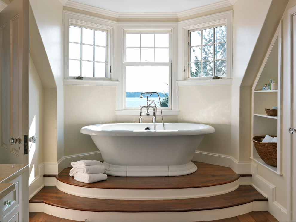 Inredning av ett klassiskt badrum, med ett fristående badkar, beige väggar och mörkt trägolv