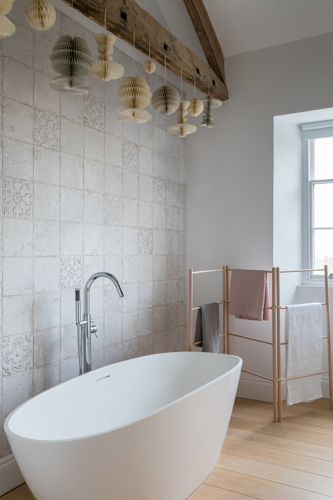 Inspiration for a medium sized contemporary ensuite bathroom in Devon with a freestanding bath, grey tiles, white walls, light hardwood flooring and beige floors.