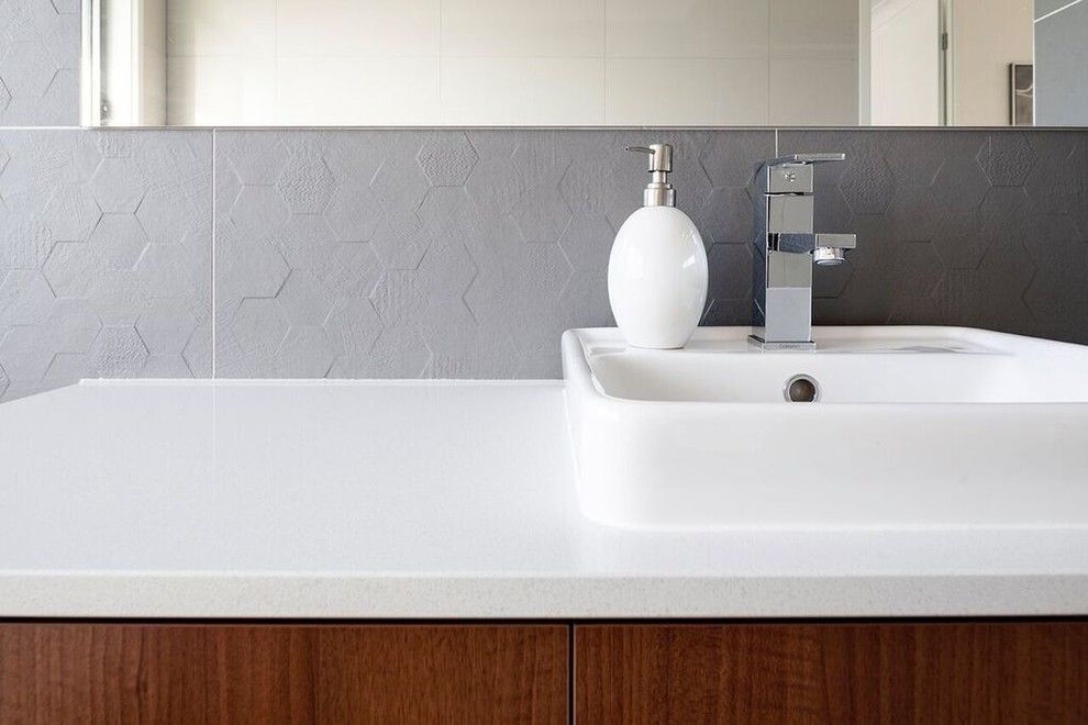 Foto di una stanza da bagno contemporanea con piastrelle grigie, piastrelle in ceramica, pareti grigie, lavabo da incasso e top in superficie solida