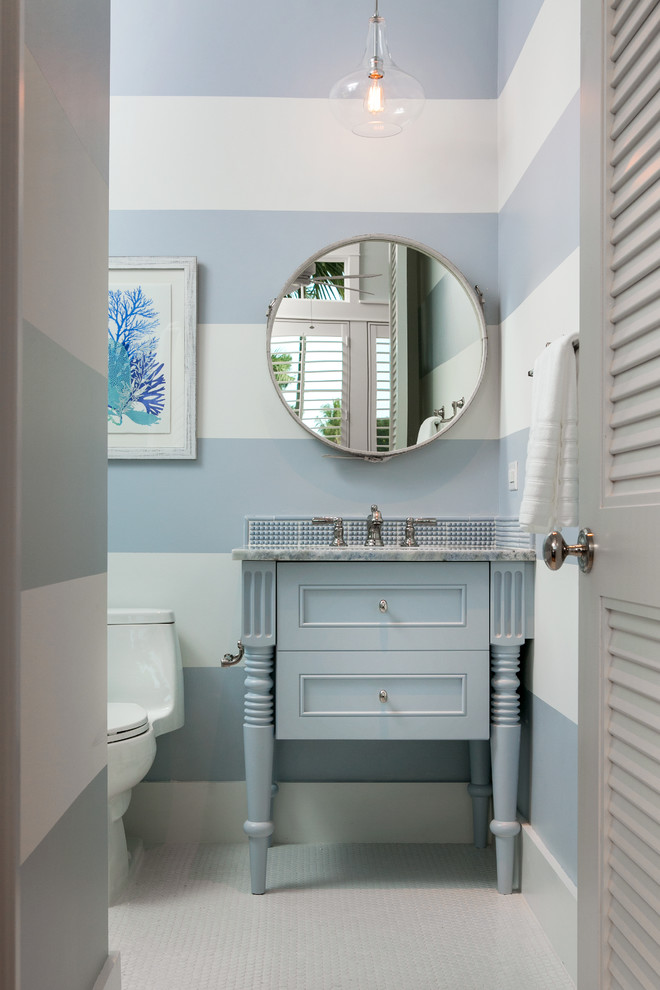 マイアミにある小さなビーチスタイルのおしゃれな浴室 (落し込みパネル扉のキャビネット、青いキャビネット、一体型トイレ	、青い壁、無垢フローリング、コンソール型シンク、大理石の洗面台、白い床) の写真
