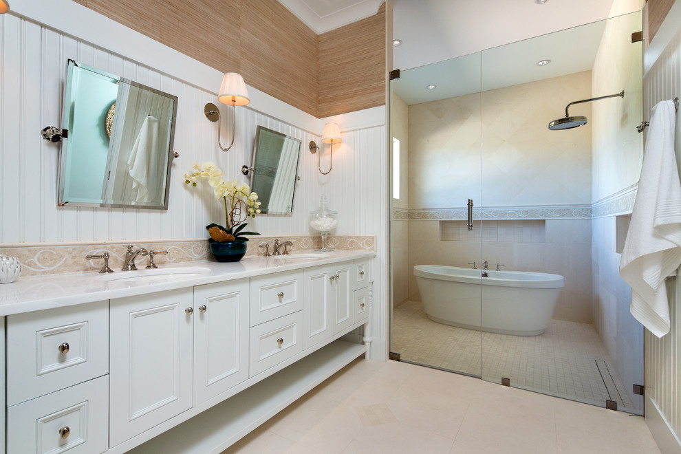Inspiration for a large coastal beige tile limestone floor and beige floor bathroom remodel in Miami with recessed-panel cabinets, white cabinets, brown walls, an undermount sink and a hinged shower door