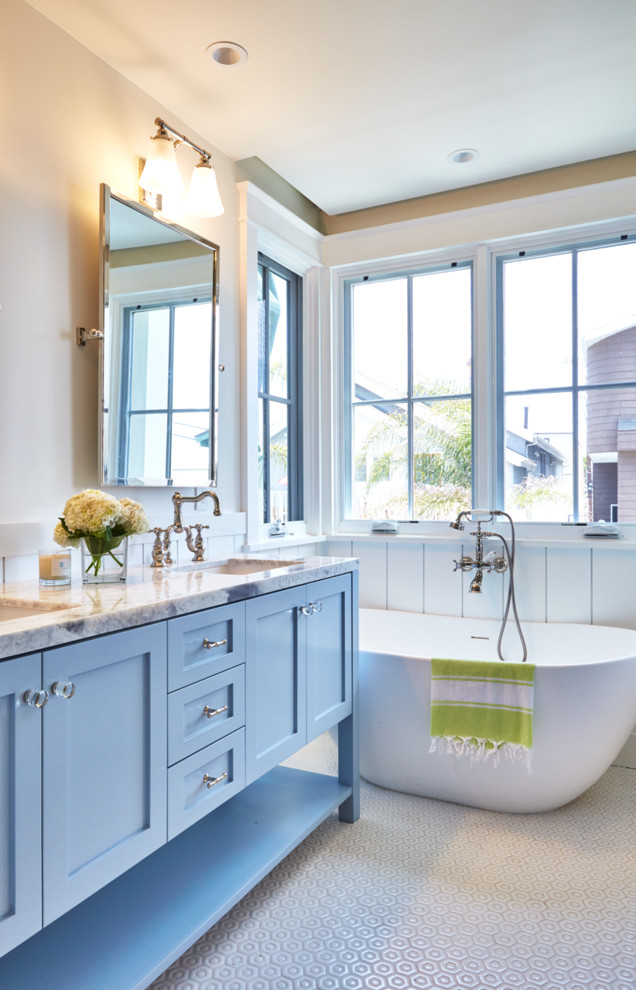 Cette photo montre une petite salle d'eau nature avec des portes de placard bleues, une baignoire indépendante, un combiné douche/baignoire, un mur blanc, un sol en bois brun et une vasque.