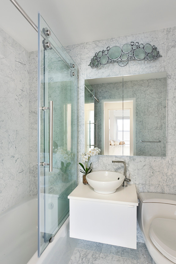 Cette image montre une petite salle d'eau design avec une vasque, un placard à porte vitrée, des portes de placard blanches, une baignoire posée, un combiné douche/baignoire, WC à poser, un carrelage gris, un mur gris et un sol en marbre.