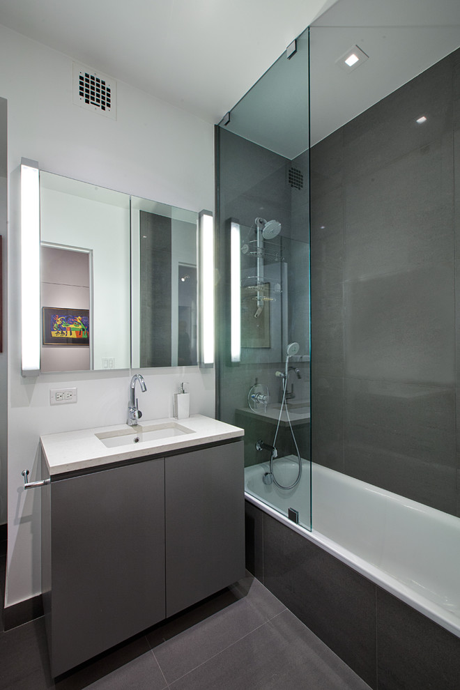 This is an example of a contemporary bathroom in New York with flat-panel cabinets, grey cabinets, a built-in bath, a shower/bath combination, grey tiles and ceramic tiles.