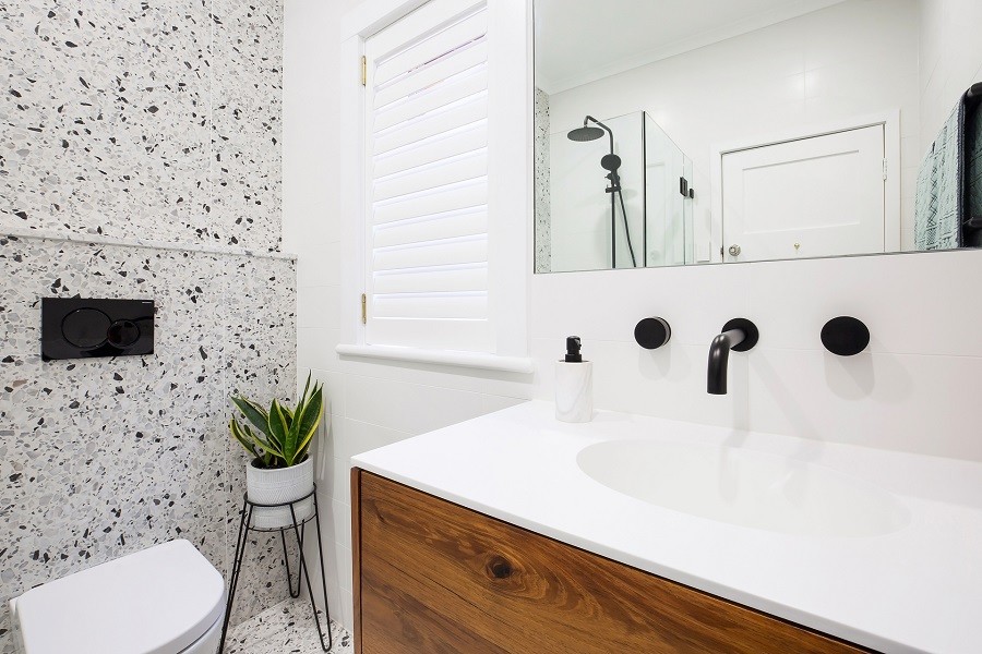 Пример оригинального дизайна: ванная комната среднего размера в стиле модернизм с фасадами островного типа, темными деревянными фасадами, душевой комнатой, инсталляцией, черно-белой плиткой, каменной плиткой, белыми стенами, полом из терраццо, душевой кабиной, монолитной раковиной, столешницей из искусственного кварца, разноцветным полом, душем с распашными дверями и белой столешницей