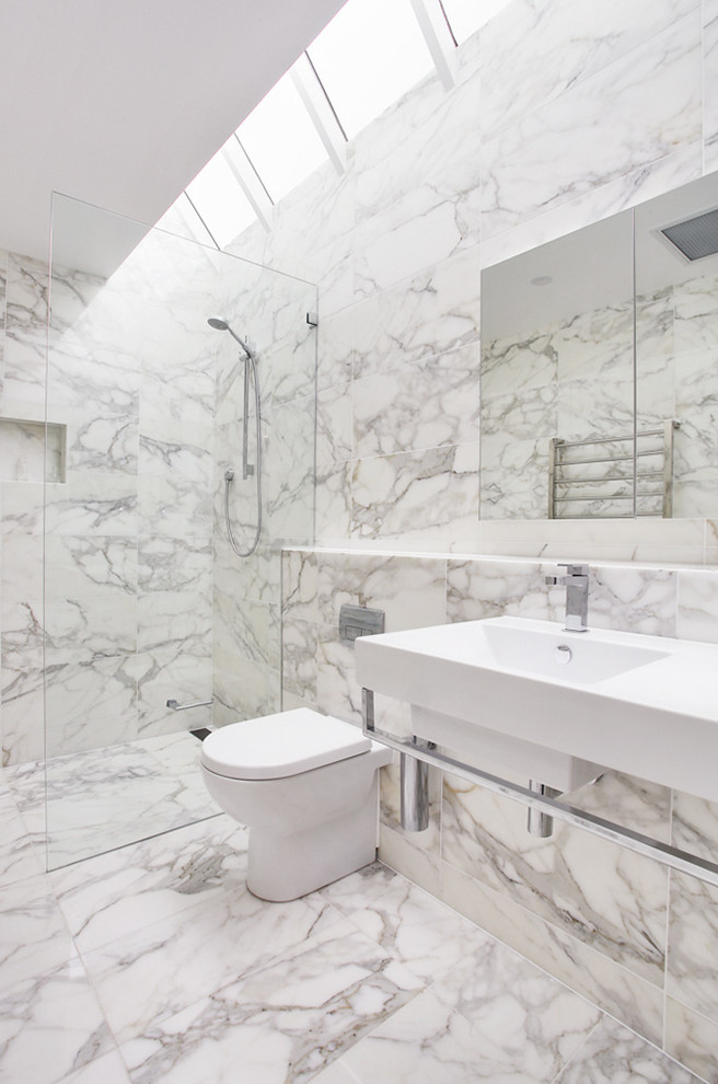 Foto på ett stort funkis en-suite badrum, med ett väggmonterat handfat, en kantlös dusch, vit kakel, vita skåp, en toalettstol med hel cisternkåpa, marmorkakel, flerfärgade väggar, marmorgolv och bänkskiva i kvartsit