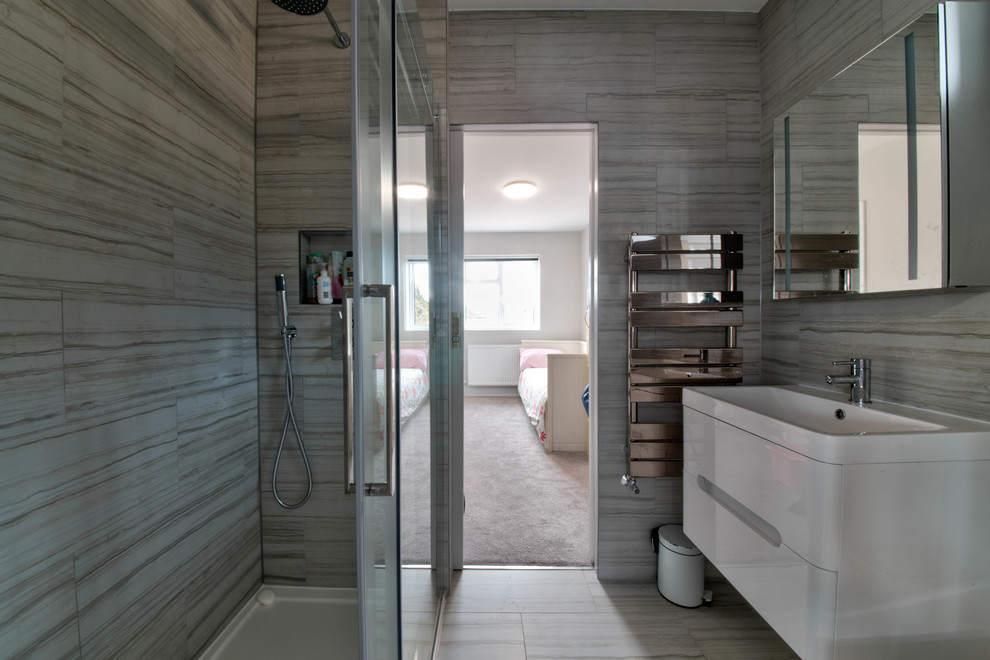 Photo of a medium sized contemporary ensuite bathroom in Surrey with flat-panel cabinets, white cabinets, a shower/bath combination, a two-piece toilet, beige tiles, ceramic tiles, beige walls, porcelain flooring, a built-in sink, multi-coloured floors and a hinged door.