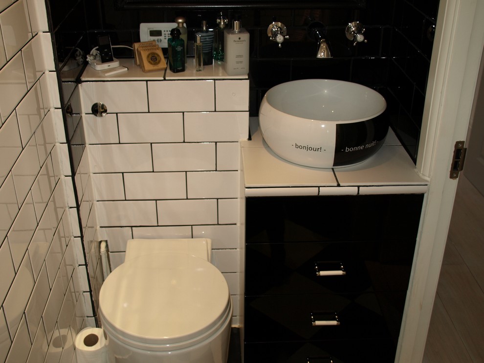 Modern inredning av ett litet badrum, med ett konsol handfat, släta luckor, svarta skåp, kaklad bänkskiva, en öppen dusch, en toalettstol med hel cisternkåpa, svart kakel, keramikplattor, vita väggar och klinkergolv i keramik
