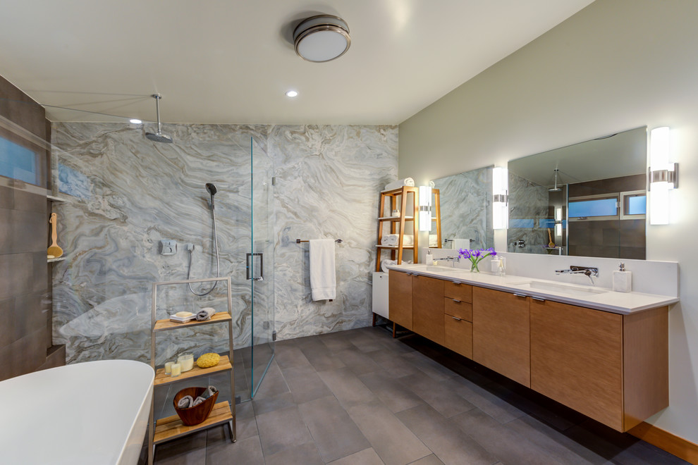 Photo of a large contemporary ensuite bathroom in San Francisco with flat-panel cabinets, light wood cabinets, a freestanding bath, a walk-in shower, grey tiles, stone slabs, a submerged sink, engineered stone worktops, a hinged door, white worktops, grey walls, ceramic flooring and grey floors.