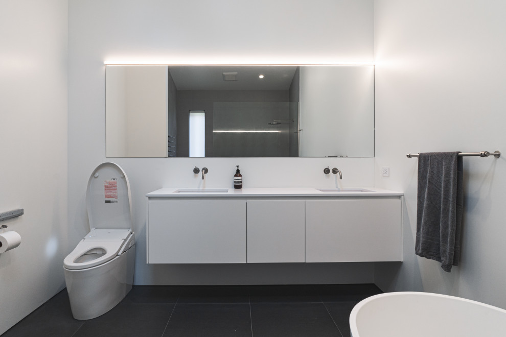 Idéer för ett stort modernt vit en-suite badrum, med släta luckor, vita skåp, ett fristående badkar, en kantlös dusch, en toalettstol med hel cisternkåpa, vita väggar, klinkergolv i keramik, ett integrerad handfat, bänkskiva i kvarts, grått golv och med dusch som är öppen