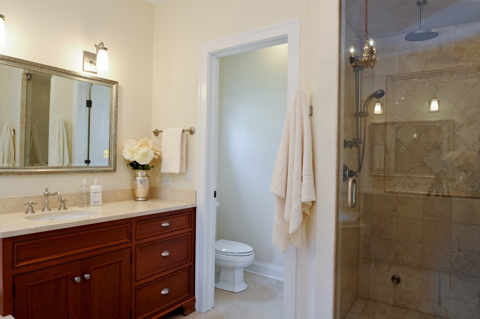 Klassisk inredning av ett mellanstort en-suite badrum, med ett undermonterad handfat, luckor med profilerade fronter, skåp i mellenmörkt trä, bänkskiva i kalksten, en dusch i en alkov, beige kakel, stenkakel, beige väggar och kalkstensgolv