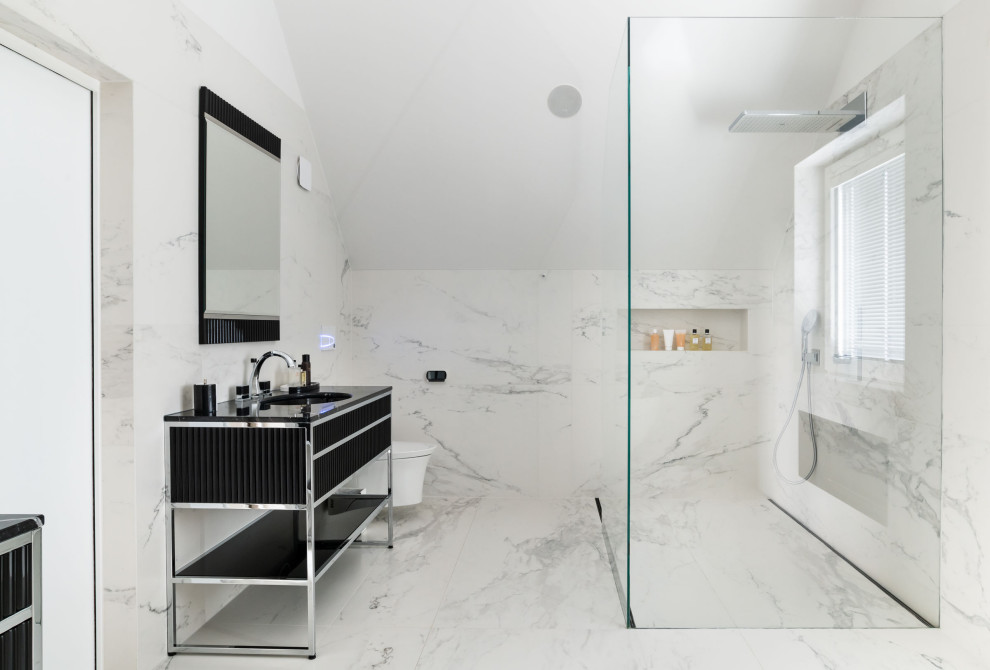 Expansive contemporary ensuite bathroom in London with black cabinets, a wall mounted toilet, white tiles, marble tiles, white walls, marble flooring, solid surface worktops, white floors, black worktops, a corner shower, a vaulted ceiling and flat-panel cabinets.